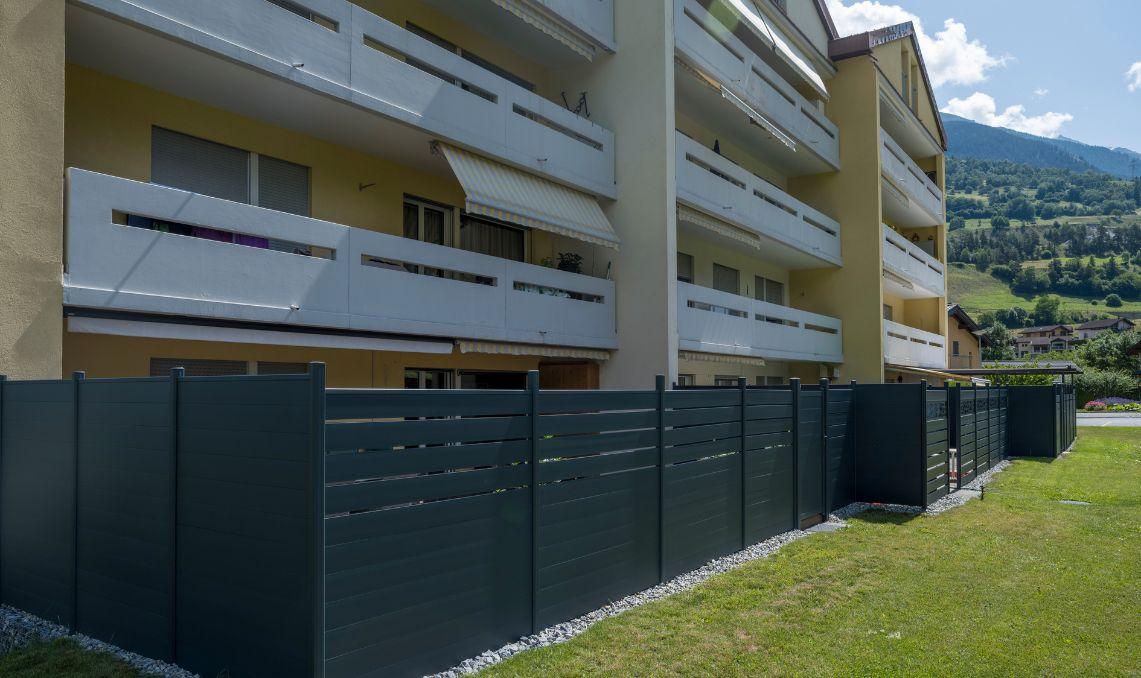 Clôture composite anthracite Silvadec pour aménagement extérieur résidentiel - Occultation de jardin en bois composite installée en alignement devant immeuble collectif