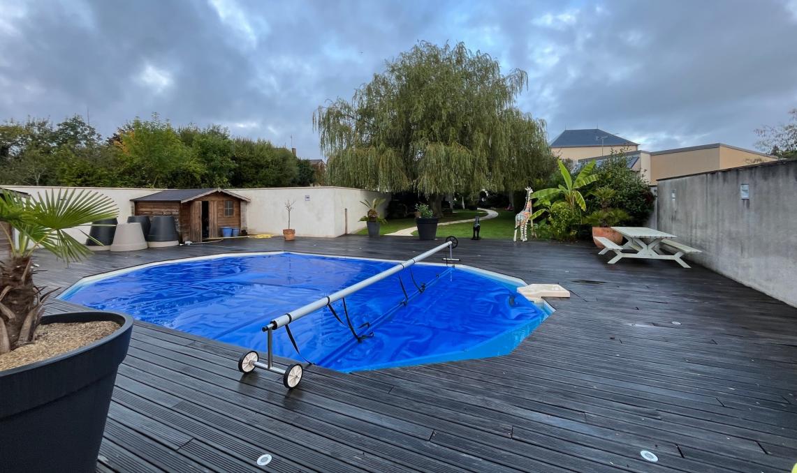 Avant travaux : terrasse composite grisaillée autour d'une piscine ovale bâchée, jardin résidentiel en Vendée